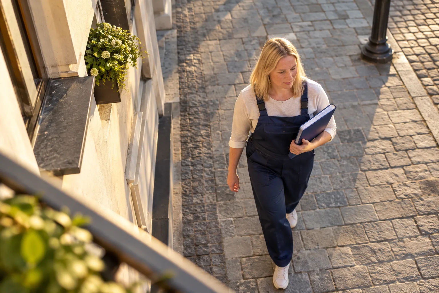 Жінка з папкою йде брукованою вулицею повз будівлі